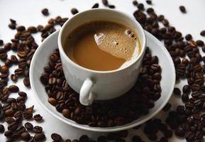 vit porslin kopp med kaffe och kaffe bönor på en vit bakgrund. te par med skummig kaffe och kaffe bönor. foto