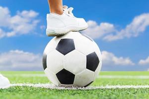 fötter av en pojke som bär vita sneakers som kliver på en fotboll. foto