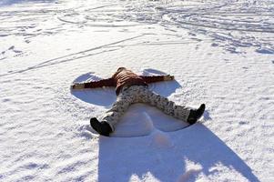 ung kvinna liggande i de snö och framställning en snö ängel. vinter- promenader och roligt foto