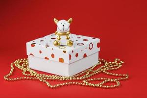 ny år 2021 leksak tjur med en gåva på en röd bakgrund. gåva låda och guld pärlor. foto