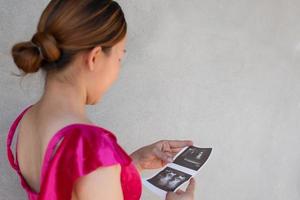 en graviditet kvinnor är se på skanna bebis bild med Lycklig leende och cement vägg bakgrund, mor och nyfödd begrepp medium skott, kopia Plats för enskild text och design foto