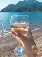 en glas av vit vin i hand på de bakgrund av hav foto
