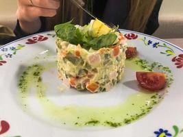 de flicka äter ryska nationell sallad olivier utsökt gott grön ärtor, korvar och potatisar på en tallrik på de tabell i en Kafé, restaurang. ryska nationell sallad foto