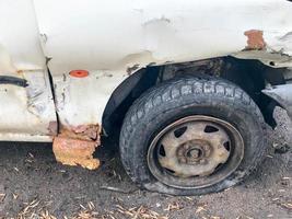 gammal vit rostig bruten bil av de kadaver med sänkt punkterad hjul med repor korrosion och en avrives stötfångare med bucklor och repor kastas på de väg. bil skräp foto