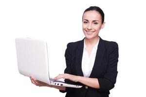 Ansluta sig en digital ålder skön ung kvinna i formell klädsel arbetssätt på bärbar dator och leende, isolerat på vit bakgrund foto