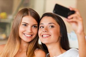 vi kärlek framställning selfie två attraktiv ung kvinnor framställning selfie förbi smart telefon foto