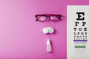 ögonläkare Tillbehör glasögon, linser och vitaminer med en testa mål för syn korrektion på en rosa bakgrund. foto