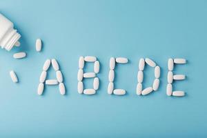 vitamin en b c d e tabletter föll ut av en vit burk på en blå bakgrund. foto