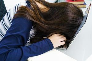 ung kvinna långt hår somnar på skrivbordet med laptop foto