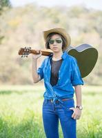 kvinna ha på sig hatt och bära henne gitarr i gräs fält foto