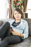 kvinna kort hår använda sig av mobil telefon på de soffa foto