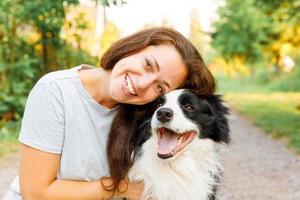 leende ung attraktiv kvinna leker med söt hundvalp border collie på sommar utomhus bakgrund. flicka håller omfamning kramar hund vän. husdjursvård och djurkoncept. foto