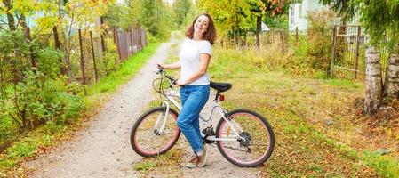 ung kvinna ridning cykel i sommar stad parkera utomhus. aktiva människor. hipster flicka koppla av och ryttare cykel. cykling till arbete på sommar dag. cykel och ekologi livsstil begrepp. foto