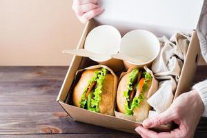 vegetarian hamburgare med färsk grönsaker och sallad i en bulle i en låda i kvinna händer foto