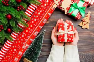 topp se av en kvinna innehav en gåva låda i henne händer på festlig trä- bakgrund. gran träd och jul dekorationer. ny år tid begrepp foto