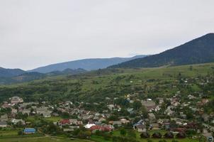 en skön se av de by av mezhgorye, karpater område. en massa av bostads- byggnader omgiven förbi hög skog bergen och lång flod foto