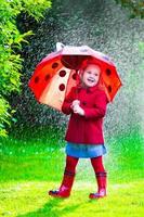 söt liten flicka med paraply som leker i regnet