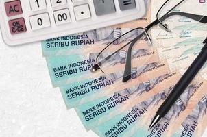 1000 indonesiska rupiah räkningar fläkt och kalkylator med glasögon och penna. företag lån eller beskatta betalning säsong begrepp foto
