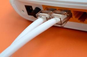 de internet kabel- pluggar är ansluten till de internet router, som lögner på en ljus orange bakgrund. objekt nödvändig för internet förbindelse foto