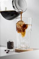 iced americano, häller de espresso i kall vatten på en vit tabell foto