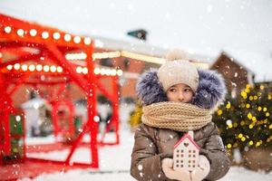 hus, miniatyr- stuga i händer av flicka bär vantar och värma kläder utomhus- i snö. familj värden, inköp hus, flytt, inteckning. mysigt Hem, jul, ny år bokning foto