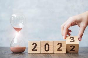 hand flip block 2022 till 2023 text med timglas på bordet. upplösning, tid, plan, mål, motivation, omstart, nedräkning och nyårssemesterkoncept foto