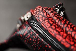 bälte väska tillverkad av texturerad, ojämn svart och röd läder på en sten mörk bakgrund. elegant svart och röd väska med en dragkedja. äkta läder, handgjort foto
