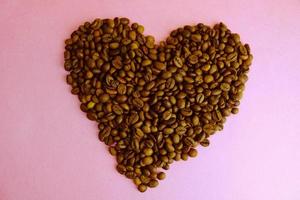 skön textur i de form av en hjärta från nyligen rostad vald utsökt mättad brun naturlig doftande arabica och robusta kaffe bönor. kopia Plats, platt lägga, rosa lila bakgrund foto
