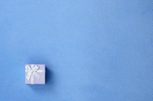 en små gåva låda i blå med en små rosett lögner på en filt av mjuk och hårig ljus blå skinna tyg. förpackning för en gåva till din härlig flickvän foto