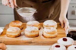 kvinna förbereder färsk munkar med sylt i Hem kök. matlagning traditionell jewish hanukkah sufganiyot. foto