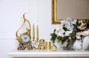 ny år och jul sammansättning. dekorativ gyllene klocka, tjock ljus, ljusstake, pott av blommor och inramade duk den där hänger på de vägg foto