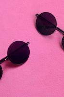 två eleganta svart solglasögon med runda glasögon lögner på en filt tillverkad av mjuk och fluffig ljus rosa skinna tyg. modern bakgrund bild i kvinna färger foto