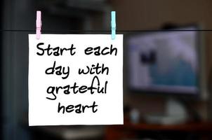 Start varje dag med tacksam hjärta. notera är skriven på en vit klistermärke den där hänger med en klädnypa på en rep på en bakgrund av kontor interiör foto