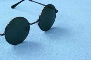 eleganta svart solglasögon med runda glasögon lögner på en filt tillverkad av mjuk och fluffig ljus blå skinna tyg. modern bakgrund bild i kvinna färger foto