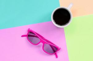 små vit kaffe kopp och rosa solglasögon på bakgrund av mode pastell rosa, blå, korall och kalk färger foto