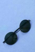 eleganta svart solglasögon med runda glasögon lögner på en filt tillverkad av mjuk och fluffig ljus blå skinna tyg. modern bakgrund bild i kvinna färger foto