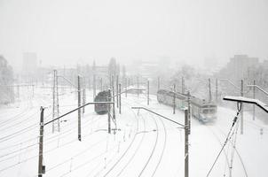 en lång tåg av passagerare bilar är rör på sig längs de järnväg Spår. järnväg landskap i vinter- efter snöfall foto