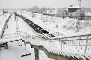 en lång tåg av frakt bilar är rör på sig längs de järnväg Spår. järnväg landskap i vinter- efter snöfall foto