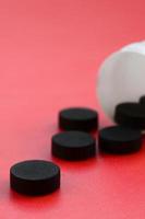 flera svart tabletter falla ut av de plast burk på de röd yta. bakgrund bild på medicinsk och farmaceutisk ämnen. aktiverad träkol foto