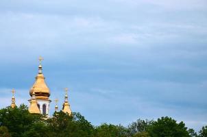 gyllene kupoler av ett ortodox kyrka bland blomstrande träd mot en bakgrund av en molnig blå himmel foto