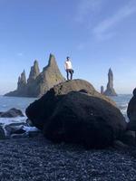 man stående på en sten på reynisfjara svart strand, Island, med vind i hans hår foto