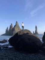 man stående på en sten på reynisfjara svart strand, Island, med vind i hans hår foto