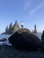 man stående på en sten på reynisfjara svart strand, Island, med vind i hans hår foto