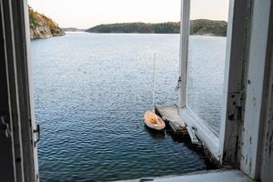 gammal öppen fönster genom som se av hav, en klippig kust, en förtöjd tätning båt och himmel på solnedgång. foto