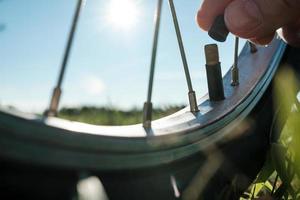 närbild av en hand med en keps från en nippel på en cykel hjul, i en äng, mot de bakgrund av de himmel. platt däck. botten se. foto