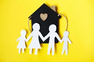 Lycklig papper skära familj innehav händer på gul bakgrund nära liten leksak hus foto