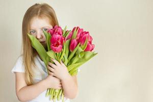 porträtt av litlle flicka med bukett av blommor tulpaner i henne händer foto