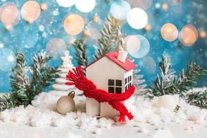 abstrakt första advent jul bakgrund. leksak hus med stickat scarf och vinter- dekorationer ornament på blå bakgrund med snö och defocused krans lampor. jul med familj på Hem begrepp. foto
