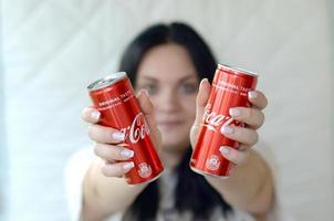 kharkov. ukraina - Maj 2, 2022 Lycklig kvinna innehav två alkoholfri Coca Cola aluminium tenn burkar i garage interiör foto