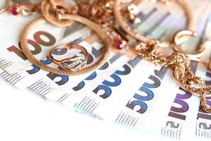 många dyr gyllene jewerly ringar, örhängen och halsband med stor belopp av ukrainska pengar räkningar. pantbank eller jewerly affär begrepp. Smycken handel foto